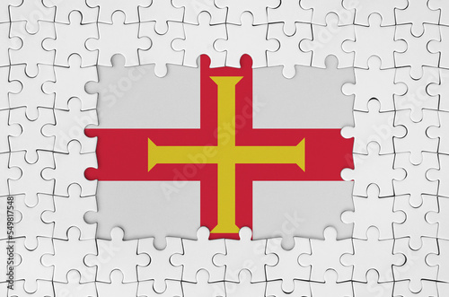 Guernsey flag in frame of white puzzle pieces with missing central part photo