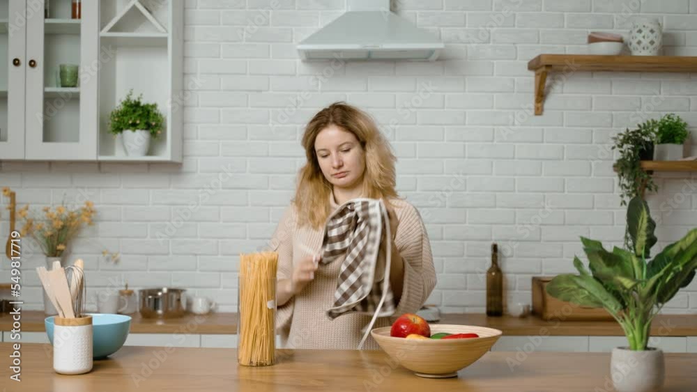 Tired housewife takes off apron after cooking and puts it on table and leaves kitchen. Woman is upset by household chores. Girl finished work and took off fabric that protects clothes from pollution Tired housewife takes off apron after cooking and puts it on table and leaves kitchen. Woman is upset by household chores. Girl finished work and took off fabric that protects clothes from pollution