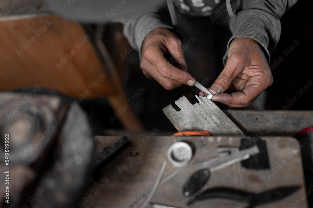 A craftsman jeweler is using a file tool to create a metal cilinder for a bracelet