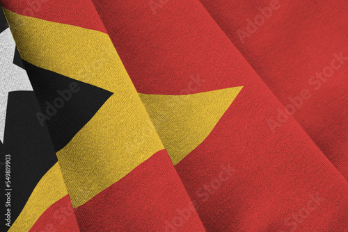Timor Leste flag with big folds waving close up under the studio light indoors. The official symbols and colors in banner photo