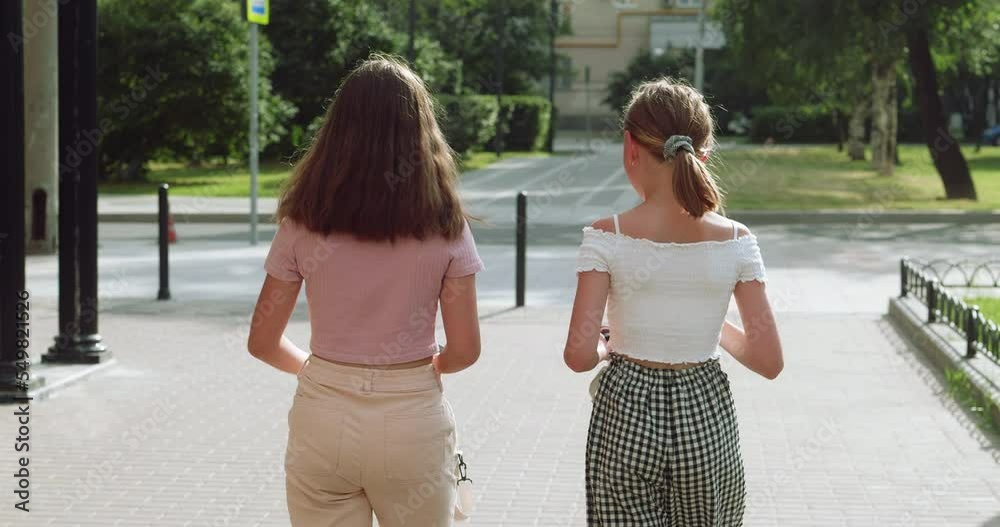 Rear view of female friends walking together. Teenage girls wearing casuals traveling on street in city. They are spending leisure time on summer weekend.