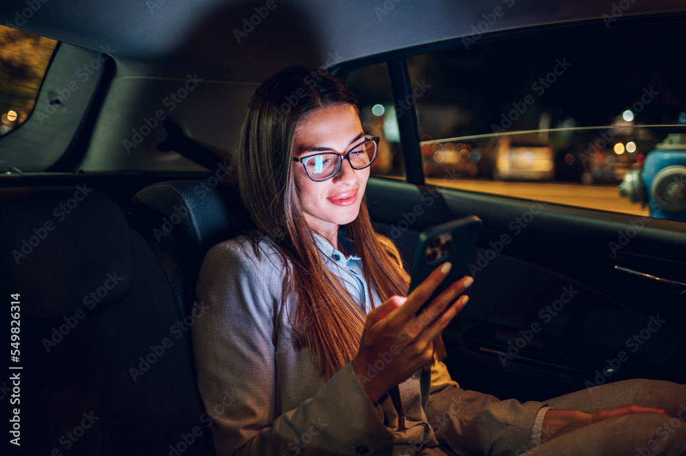 Business woman using smartphone while sitting in a backseat of a car at night Business woman using smartphone while sitting in a backseat of a car at night