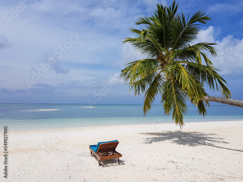 sunbed on empty tropical beach under palm tree, clear white sand in lagoon near blue water, luxury resort 