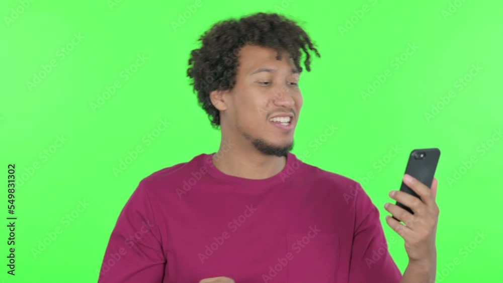 African Man Celebrating on Smartphone on Green Background