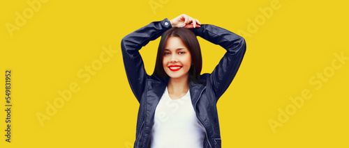 Fashionable portrait of beautiful smiling young brunette woman model posing in black leather jacket on yellow background © rohappy