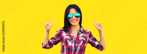 Portrait of beautiful happy smiling young brunette woman in sunglasses on yellow background
