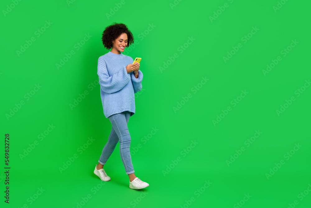 Full length photo of funny wavy lady look telephone go wear pullover jeans boots isolated on green color background Full length photo of funny wavy lady look telephone go wear pullover jeans boots isolated on green color background