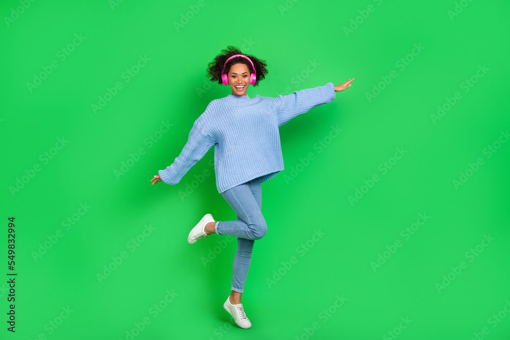 Full body photo of cheerful charming girl jump have good mood listen favorite song isolated on green color background Full body photo of cheerful charming girl jump have good mood listen favorite song isolated on green color background