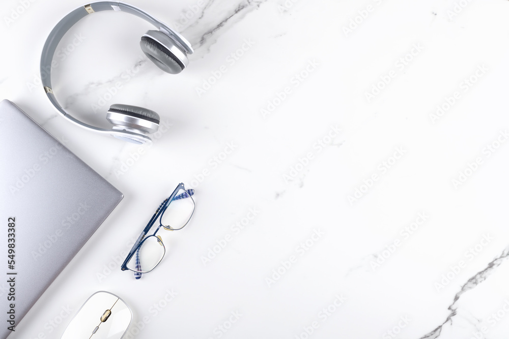 Modern office workspace with laptop, mouse, eye glasses and headphone. Business concept flat lay on white marble background. Digital communication. Creativity and innovation concept, copy space