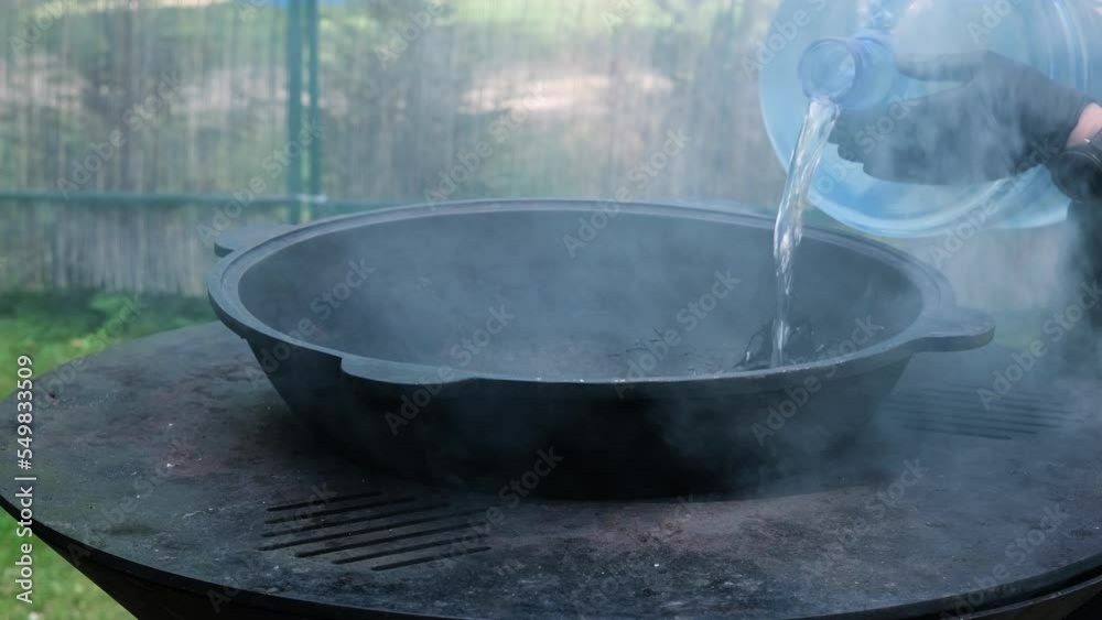 Water is added to the cauldron to boil the soup. The boiler stands on a metal grill. Slow motion horizontal video Water is added to the cauldron to boil the soup. The boiler stands on a metal grill. Slow motion horizontal video