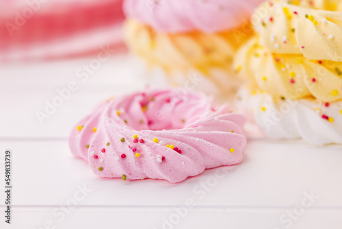 Different colors meringues with sprinkles on white table.