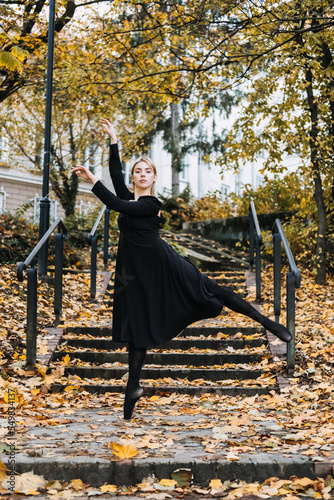 Ballerina Dancing in autumn city street, Modern Ballet Dancer in black dress, Pointe Shoes outdoors. Ballerina stretches, daily ballet stretching routine