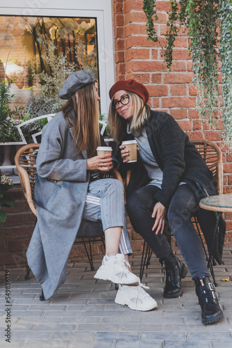Portrait young female best friends talking to each other discussing interesting themes during free time hipster girls joking and having fun together enjoying recreation with coffee to go on urban