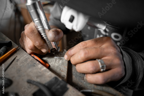 A craftsman jeweler is making small holes using the drill wearing protection glasses