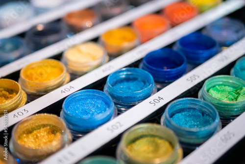 Colorful mineral eyeshadow in plastic cosmetic jars in row on counter for sale in makeup store, exhibition - close up, selective focus. Glamour, fashion, make up, beauty and skincare concept