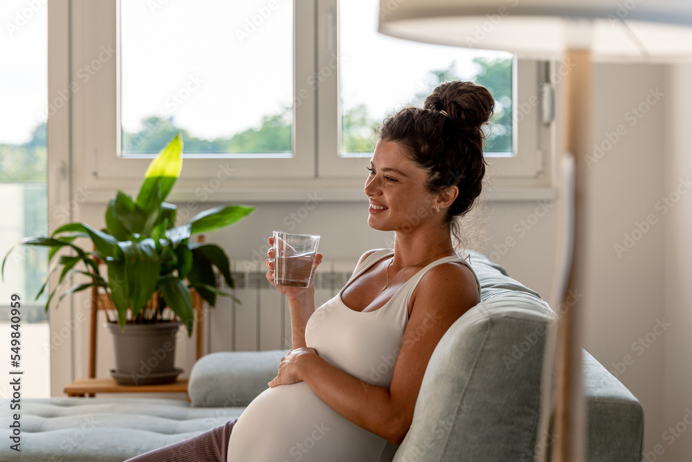 Pregnant woman drinking water on sofa at home