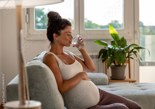 Pregnant woman drinking water on sofa at home photo