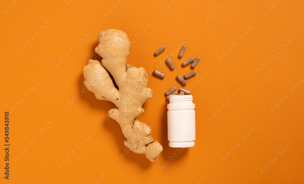Fresh ginger root jar with vitamin pills orange background, medicine, nutritional supplements