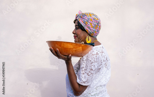 Caribbean woman wearing headwrap holding a bowl of sugar cane