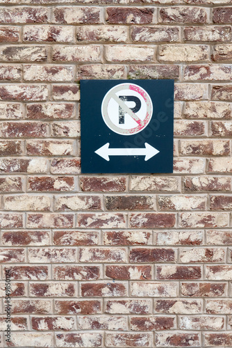 a weathered No Parking sign and two way arrows on a faded metal notice hung on a brick wall along a building downtown in an upscale urban area of the city near retail shopping and dining  photo