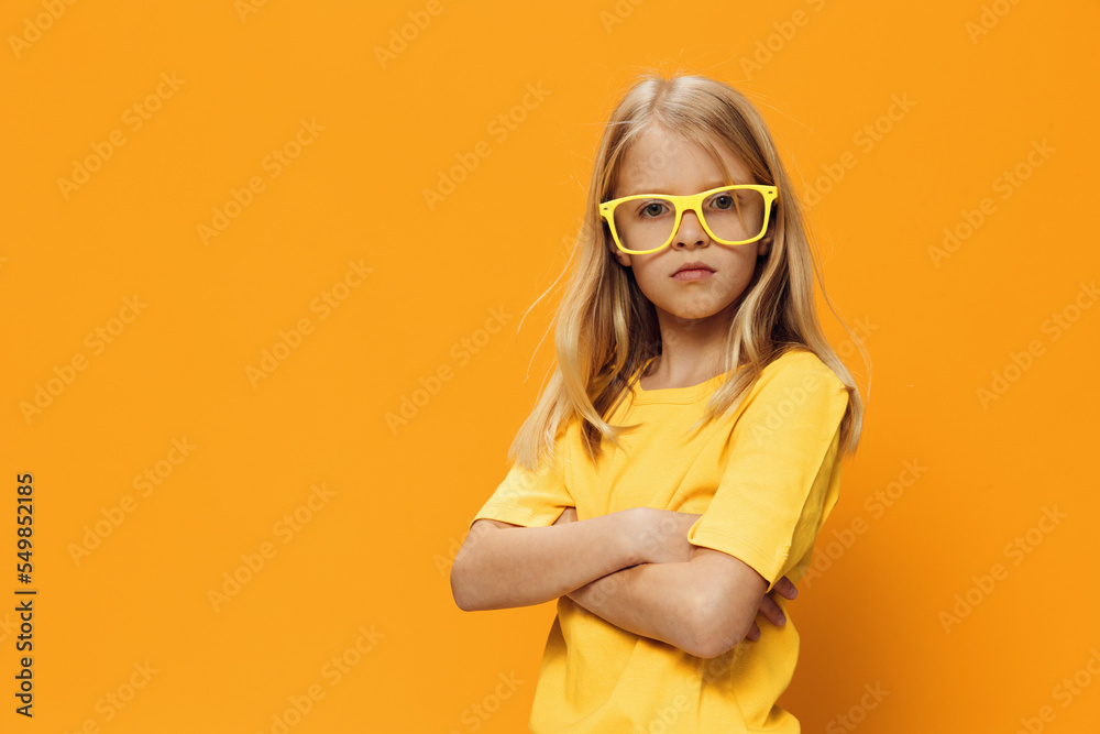 a serious concentrated girl in yellow glasses for vision stands with her arms folded on her chest. Horizontal photo on a yellow background with empty space for an advertising layout a serious concentrated girl in yellow glasses for vision stands with her arms folded on her chest. Horizontal photo on a yellow background with empty space for an advertising layout