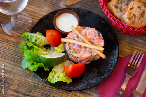 Popular appetizer of French cuisine is salmon tartare with onion cream, served with sliced tomato, lime, lettuce and sauce photo