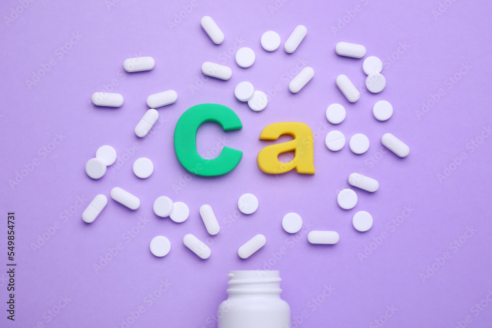 Symbol Ca (Calcium), medical bottle and pills on violet background, top view Symbol Ca (Calcium), medical bottle and pills on violet background, top view