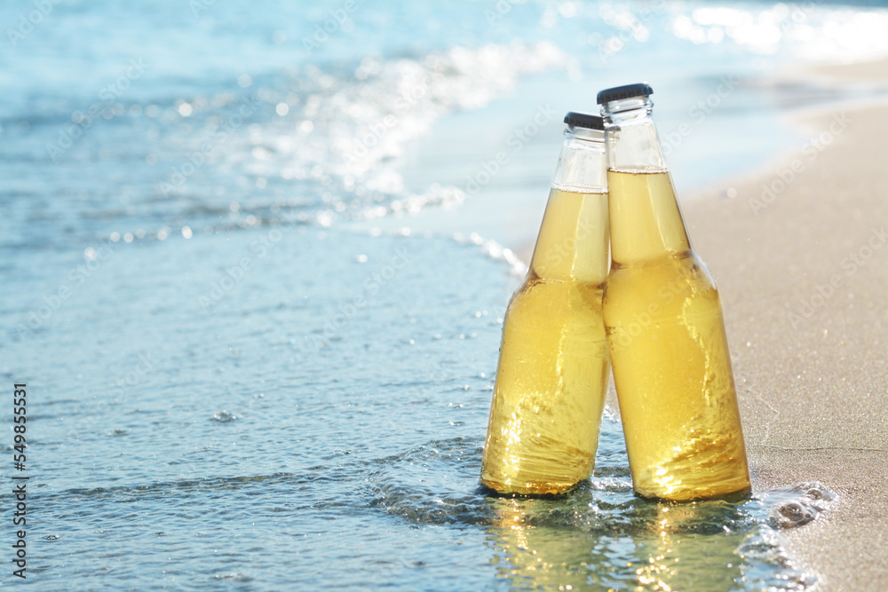 Bottles of cold beer on sandy beach near sea, space for text Bottles of cold beer on sandy beach near sea, space for text