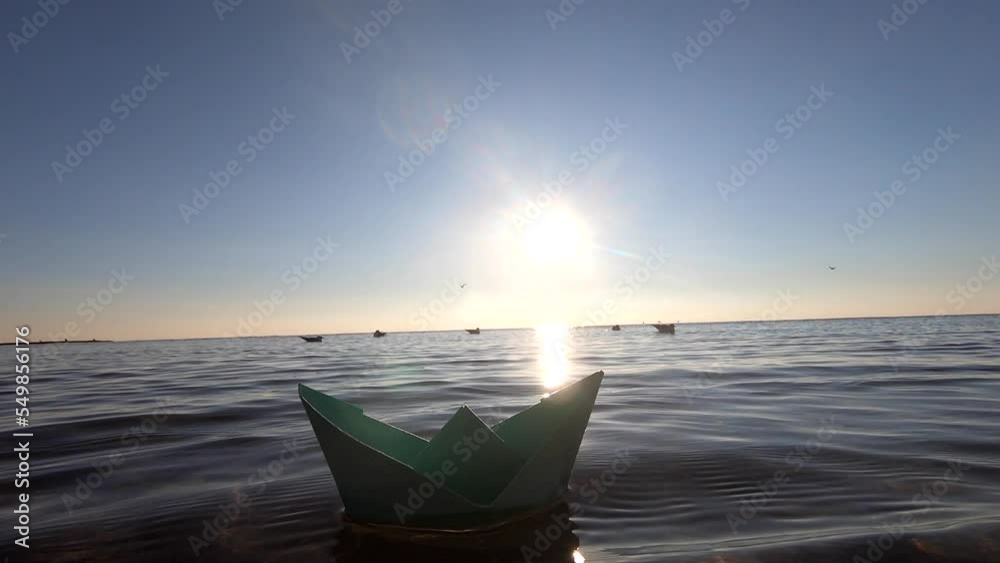 Small green paper boat floating on sea waves on summer sunny day close-up. Transparent water, shining sun, cloudless clean blue sky, sunny path. Sunny path, glare. Concept travel goal tourism dreaming Small green paper boat floating on sea waves on summer sunny day close-up. Transparent water, shining sun, cloudless clean blue sky, sunny path. Sunny path, glare. Concept travel goal tourism dreaming