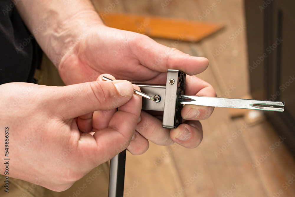The craftsman holds a door handle and a hex key in his hands, installing a door handle.