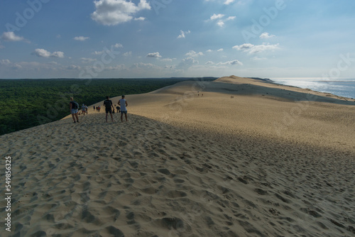 Tourists standing on Dune du Pilat, the biggest sand dune in Europe with the pine forest and view at the sea, Arcachon, Nouvelle-Aquitaine, France
