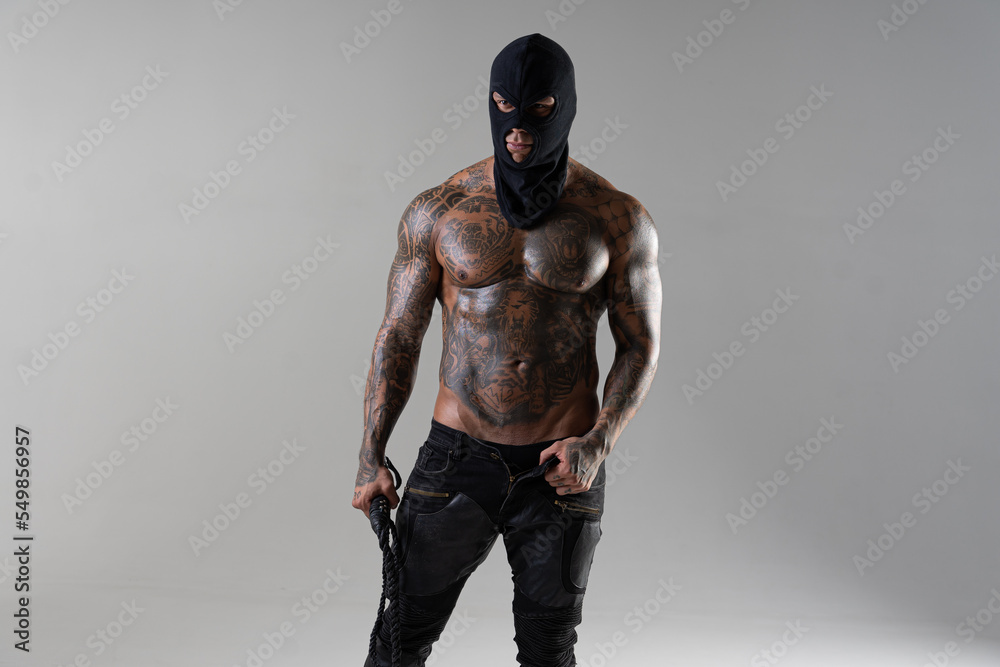 Muscular shirtless young man with whip in a mask.Brutal handsome man with tattooed body. Men tattoo casual fashion. Portrait of handsome male model. Muscular athletic sexy male with naked torso.