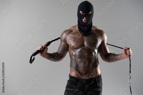 Muscular shirtless young man with whip in a mask.Brutal handsome man with tattooed body. Men tattoo casual fashion. Portrait of handsome male model. Muscular athletic sexy male with naked torso.