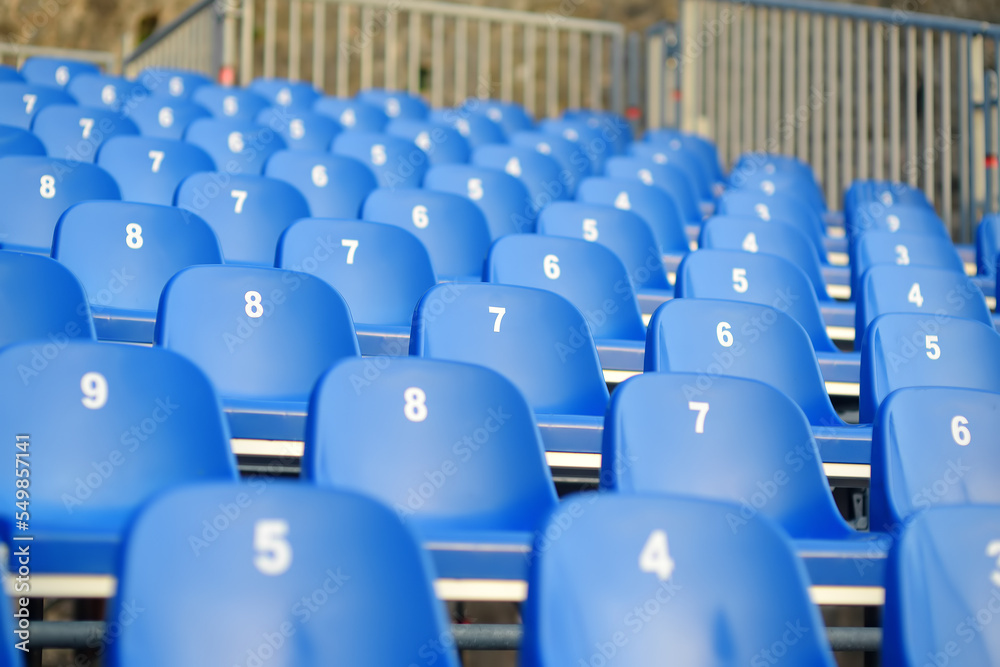 Fototapeta premium View of empty seats with numbers in the stands. Arena stands are waiting for crowds of fans. Theater, concert hall, audience are ready to start of the performance, lecture or conference.