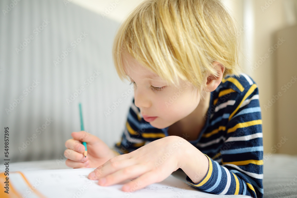 Elementary student boy doing homework at home. Child learning to count, solves arithmetic examples, doing exercises in workbook. Math tutorial. Preparing preschooler baby for school. Education Elementary student boy doing homework at home. Child learning to count, solves arithmetic examples, doing exercises in workbook. Math tutorial. Preparing preschooler baby for school. Education