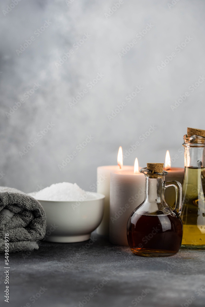 Spa massage relax composition setting. Natural essence oils, sea salt, towel, candles on gray background. Spa massage relax composition setting. Natural essence oils, sea salt, towel, candles on gray background.