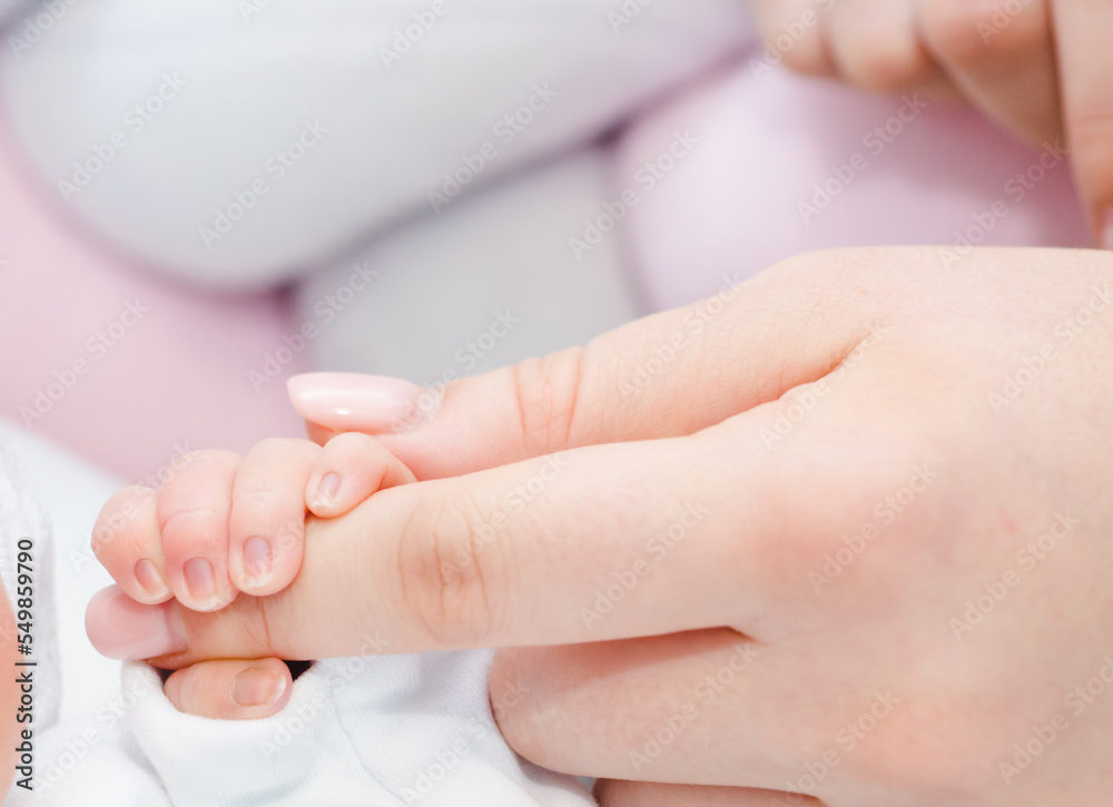 Newborn baby touching his mother hand. Mother uses her hand to hold her baby's tiny hand to make him feeling her love, warm and secure. Concept of child care, feeling safe, parent love. Newborn baby touching his mother hand. Mother uses her hand to hold her baby's tiny hand to make him feeling her love, warm and secure. Concept of child care, feeling safe, parent love.