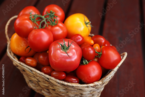 Wicker basket with fresh tomatoes on wooden table, closeup
