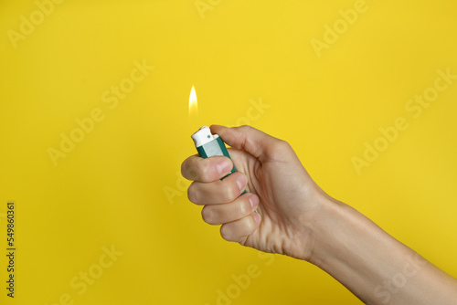 Woman holding green lighter on yellow background, closeup