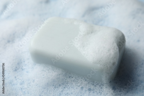 Soap with fluffy foam on light blue background, closeup