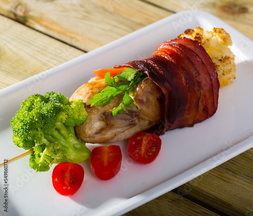 Grilled quail with jamon, fried on skewers with brocolli and tomatoes at plate