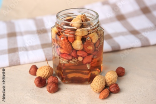 Jar with different nuts and honey on beige table