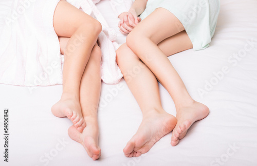 Legs of two girls in bathrobes lying in bedroom bed after shower