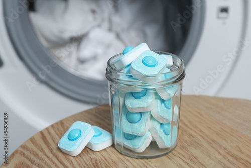 Jar with water softener tablets on wooden table near washing machine photo