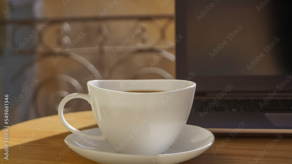 Cup of aromatic coffee and laptop on wooden table outdoors, closeup