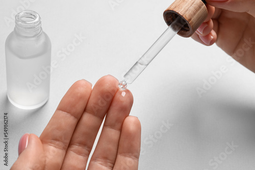 Woman dripping serum from pipette on her hand at white table  closeup