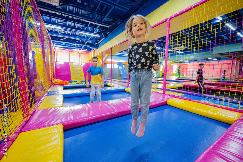 Happy kids playing at indoor play center playground. Girl ljumping on  trampoline. Photos | Adobe Stock