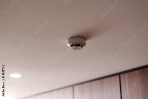 Fire system indoors. White smoke detector issue a signal to a fire alarm control panel as part of a fire alarm system installed on the white ceiling in the office building or apartment.