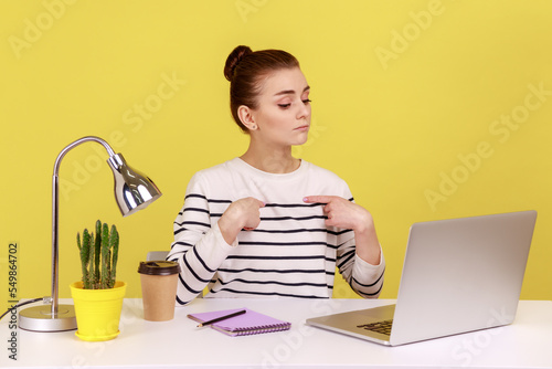 This is me. Self confident egoistic woman worker pointing herself and looking at laptop screen with arrogant expression, working in office. Indoor studio studio shot isolated on yellow background. photo