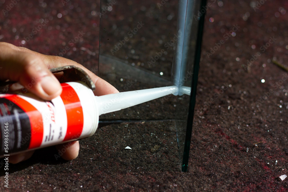 The craftsman's hand uses a silicone adhesive to connect the glass to